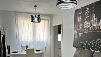 Un salon moderne avec un canapé gris, une table basse et un coin repas comprenant une table et des chaises blanches.