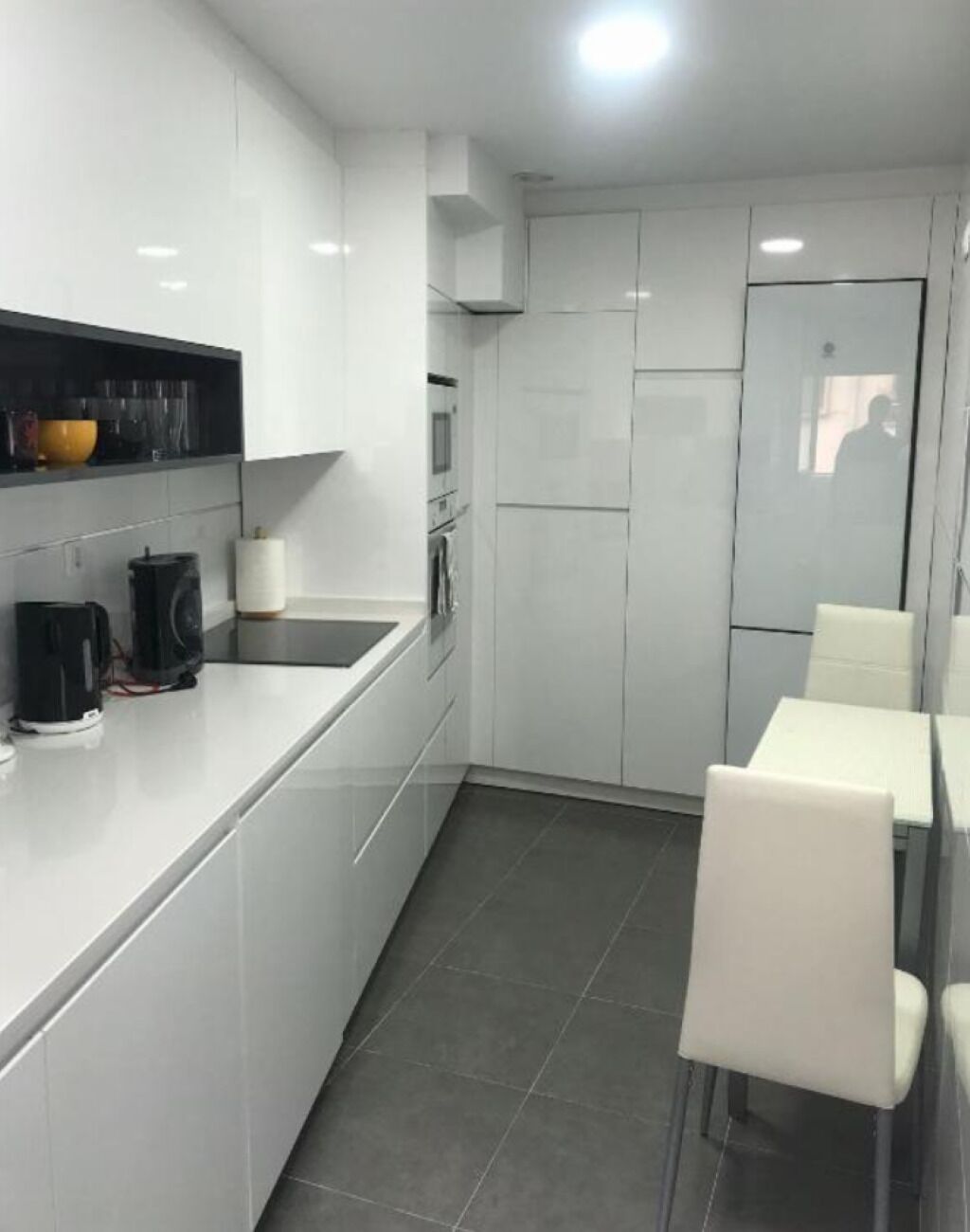 A modern kitchen with white cabinets, a black countertop, and a dining area with white chairs.