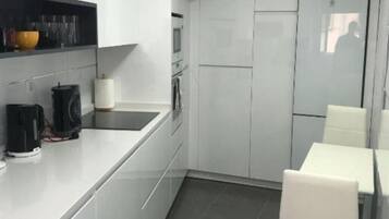 A modern kitchen with white cabinets, a black countertop, and a dining area with white chairs.