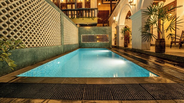 A swimming pool with a geometric wall design, a wooden deck, and a staircase leading to an upper level. - Beautiful villa with pool in charming Galle (Galle)