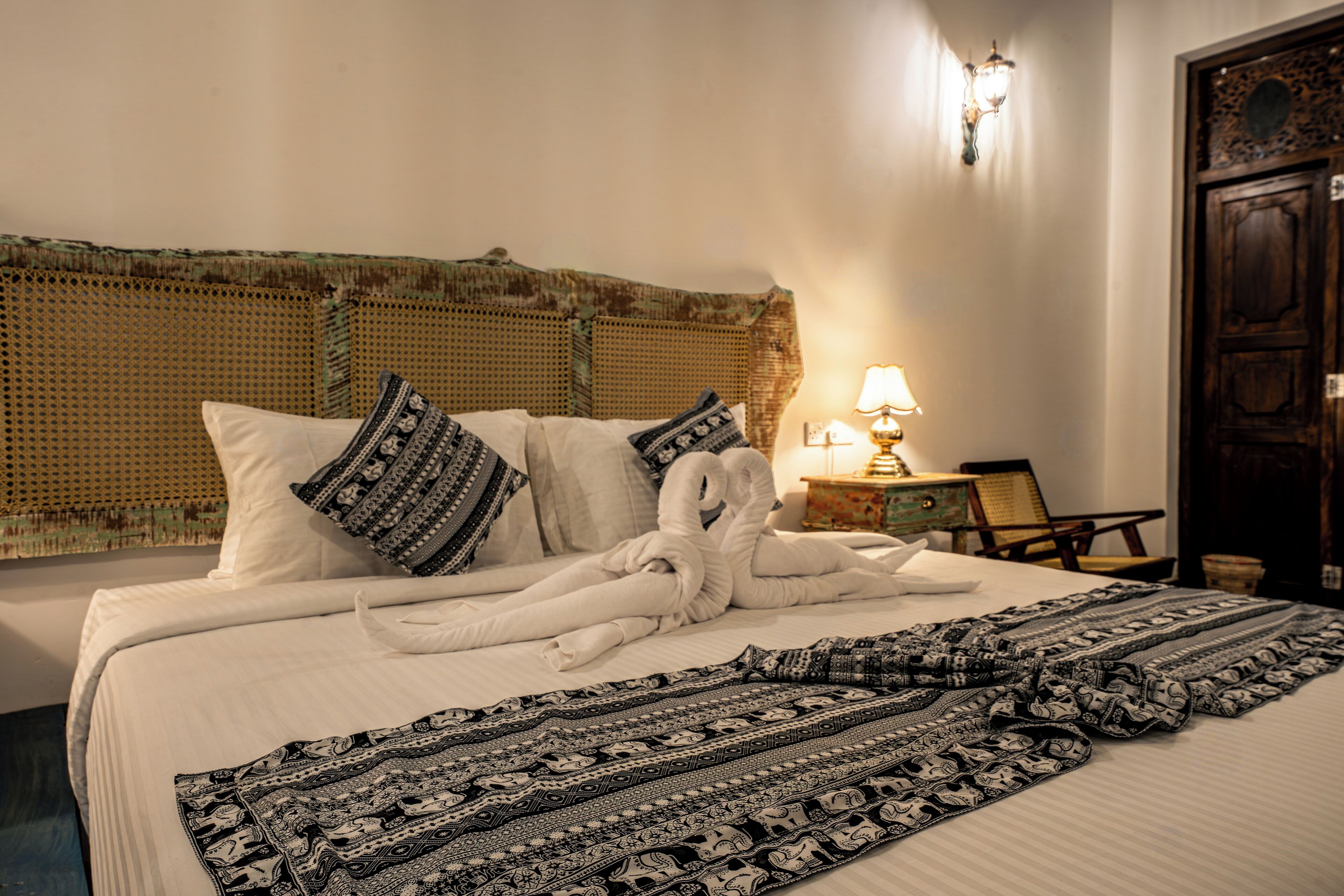 A neatly made bed with patterned blankets and pillows, a bedside lamp, and a wicker headboard.