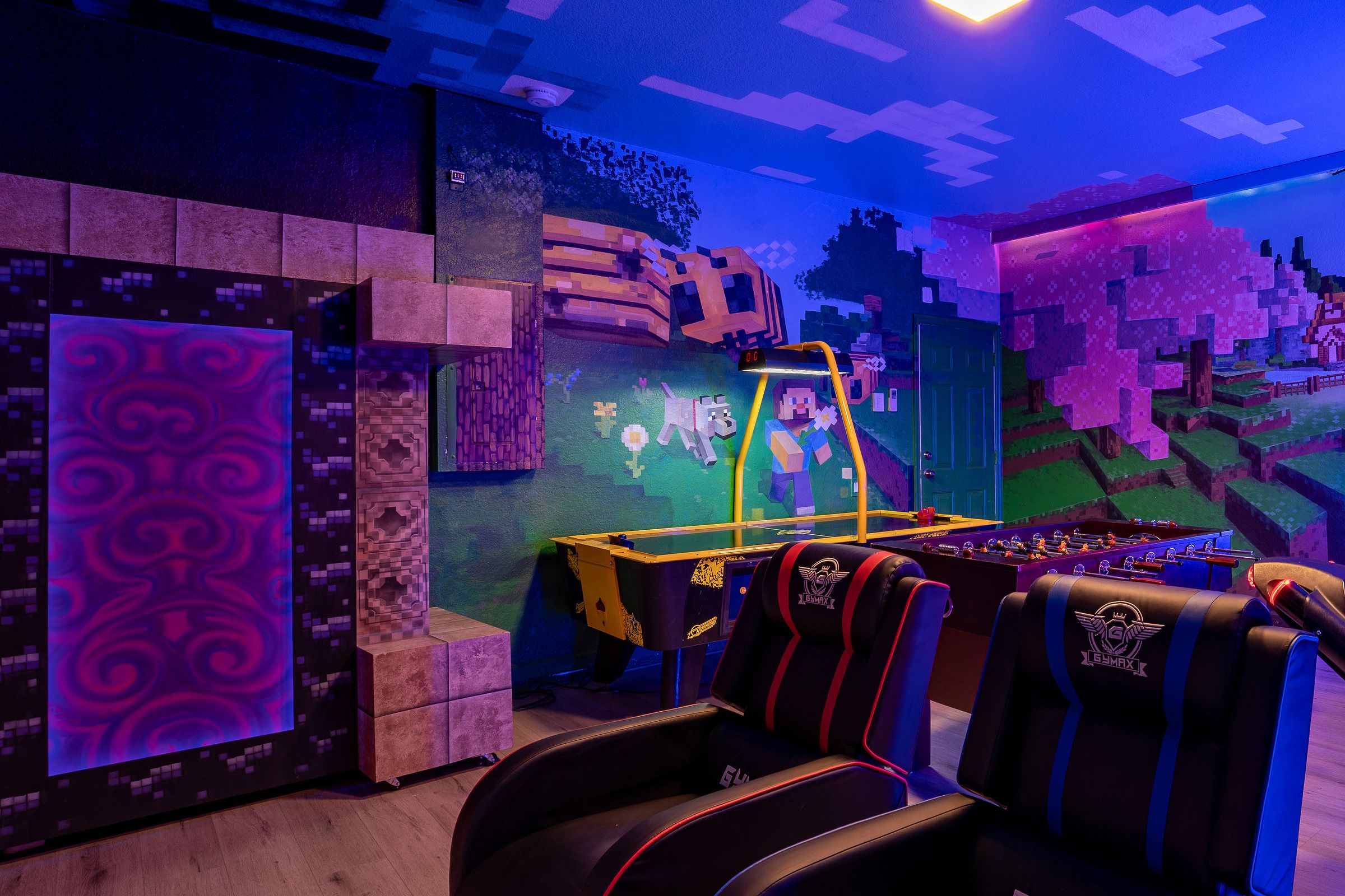 A room with a foosball table, gaming chairs, and a wall with a Minecraft-themed mural.