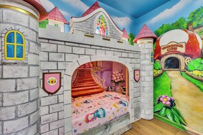 Un salón de juegos con temática de castillo, con una cama, una ventana y una puerta.