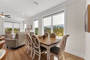 A dining area with a wooden table and chairs, large windows with blinds, and a ceiling fan. - Cape San Blas Home, Sleeps 12 w/ Yoga Station (Port St. Joe)