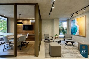 A modern office space with a meeting area, comfortable seating, a large artwork, and a view through a glass door. - Enjoy Salvador between the sea and Shopping Barra (Salvador)