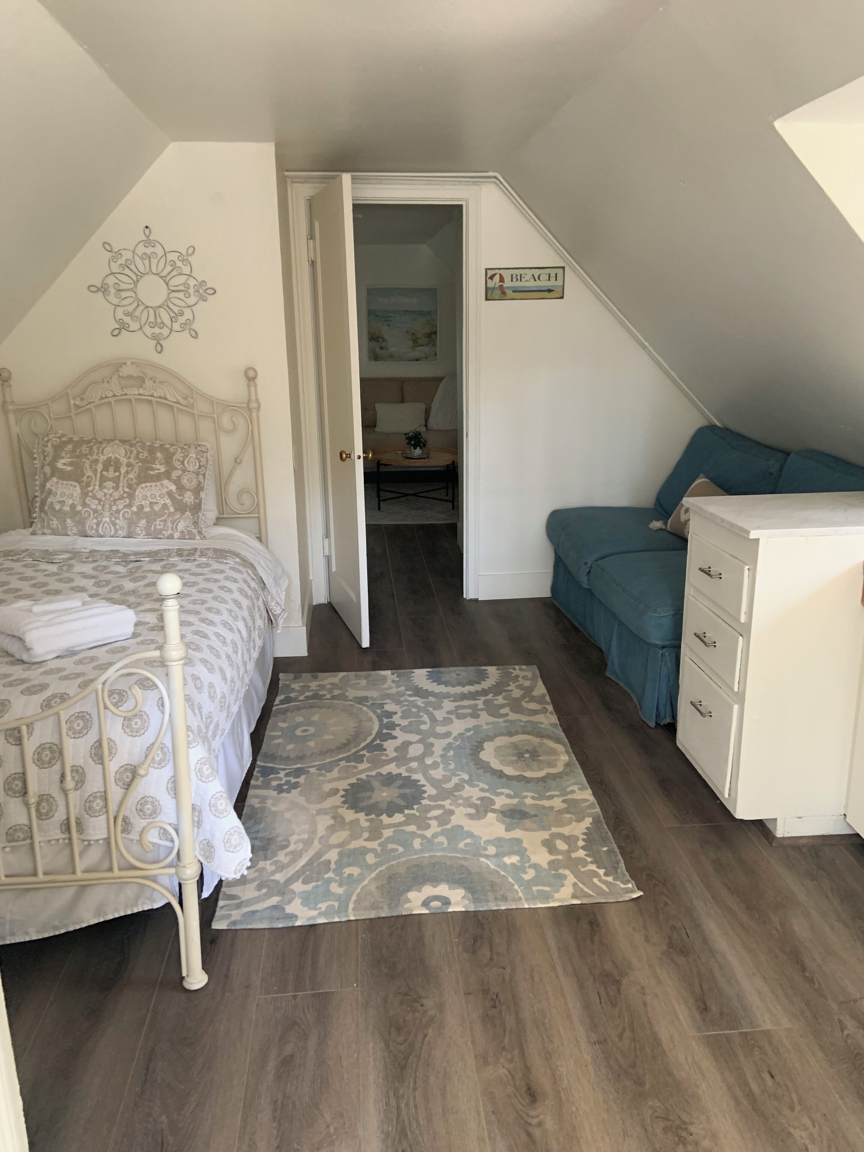 Een slaapkamer met een bed, een dressoir, een blauwe bank en een gang naar een andere kamer.
