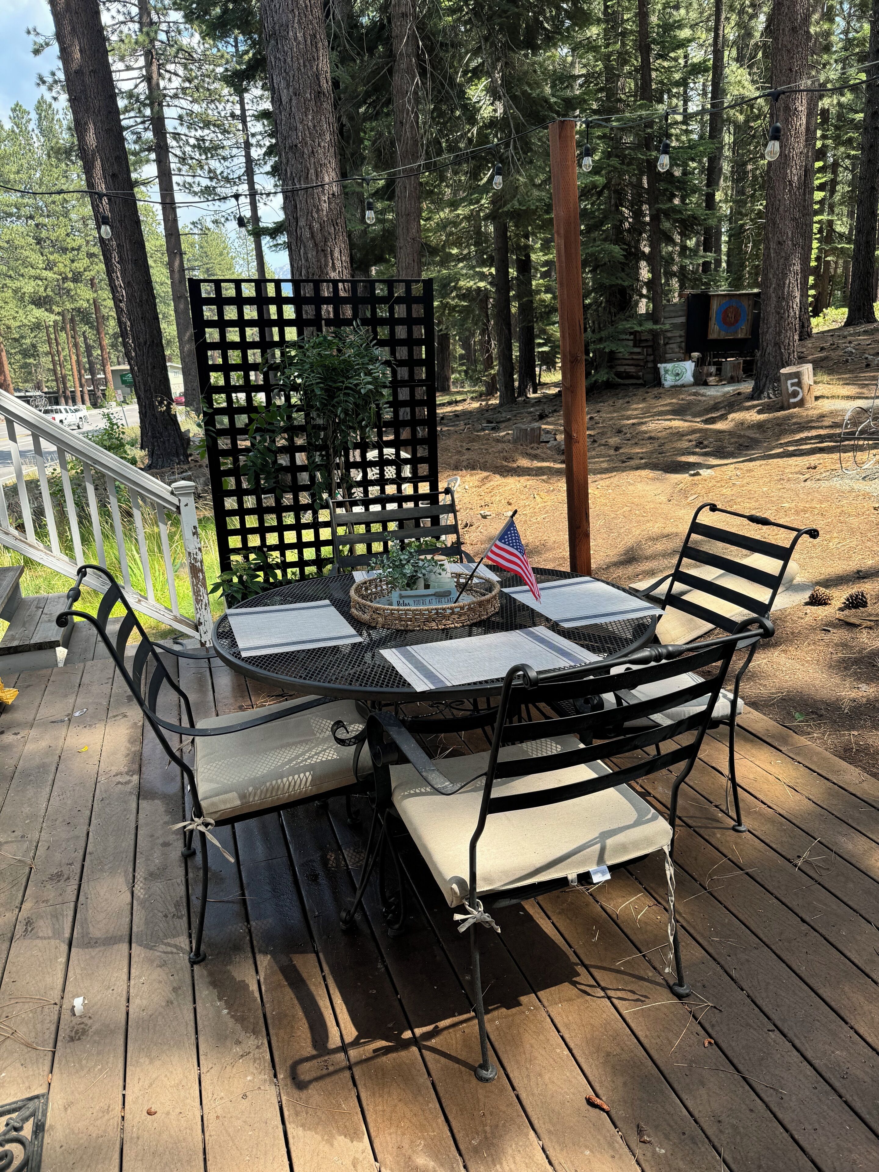 An outdoor wooden deck with a metal table and chairs, surrounded by a wooden fence and trees.