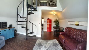 Un salon moderne avec un escalier en colimaçon, un réfrigérateur rouge, un canapé en cuir et un tapis à motifs.
