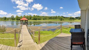 Une terrasse en bois menant à un belvédère situé au bord d’un lac, avec une barrière en corde et des chaises en osier.