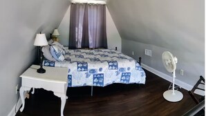 Une chambre à coucher avec un lit, une table de chevet, une lampe et un ventilateur sur pied.