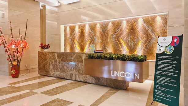 A modern reception desk with a marble finish and a 'LINCOLN' sign, a decorative wall with a marbled pattern, and a signboard with information. - Apartment Lincoln Podomoro Delipark (Medan)