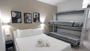 Een hotelkamer met een eenpersoonsbed, twee aan de muur bevestigde kunstwerken en een stapelbed met matrassen voorzien van plastic.