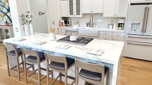 Een moderne keuken met een groot eiland, witte kastjes, roestvrijstalen apparatuur en houten stoelen.