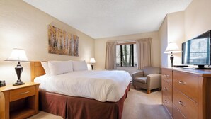 Ein Hotelzimmer mit einem großen Bett, einem Schreibtisch mit Lampe, einem Sessel, einem Schrank und einem Fernseher.