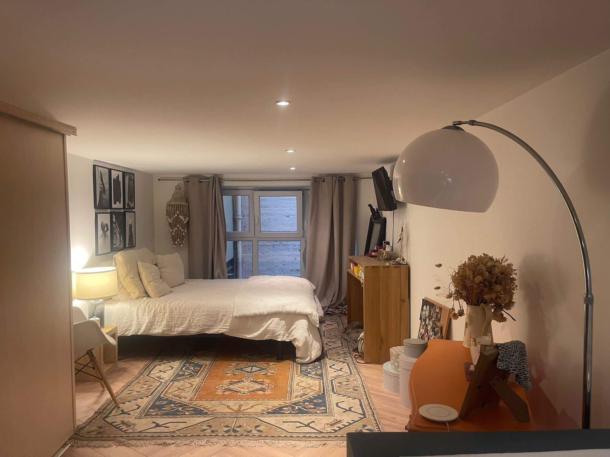 A bedroom with a bed, a desk, a chair, a lamp, a mirror, and a window.