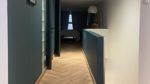 A hallway with a herringbone floor leading to a bedroom with a bed and a window.