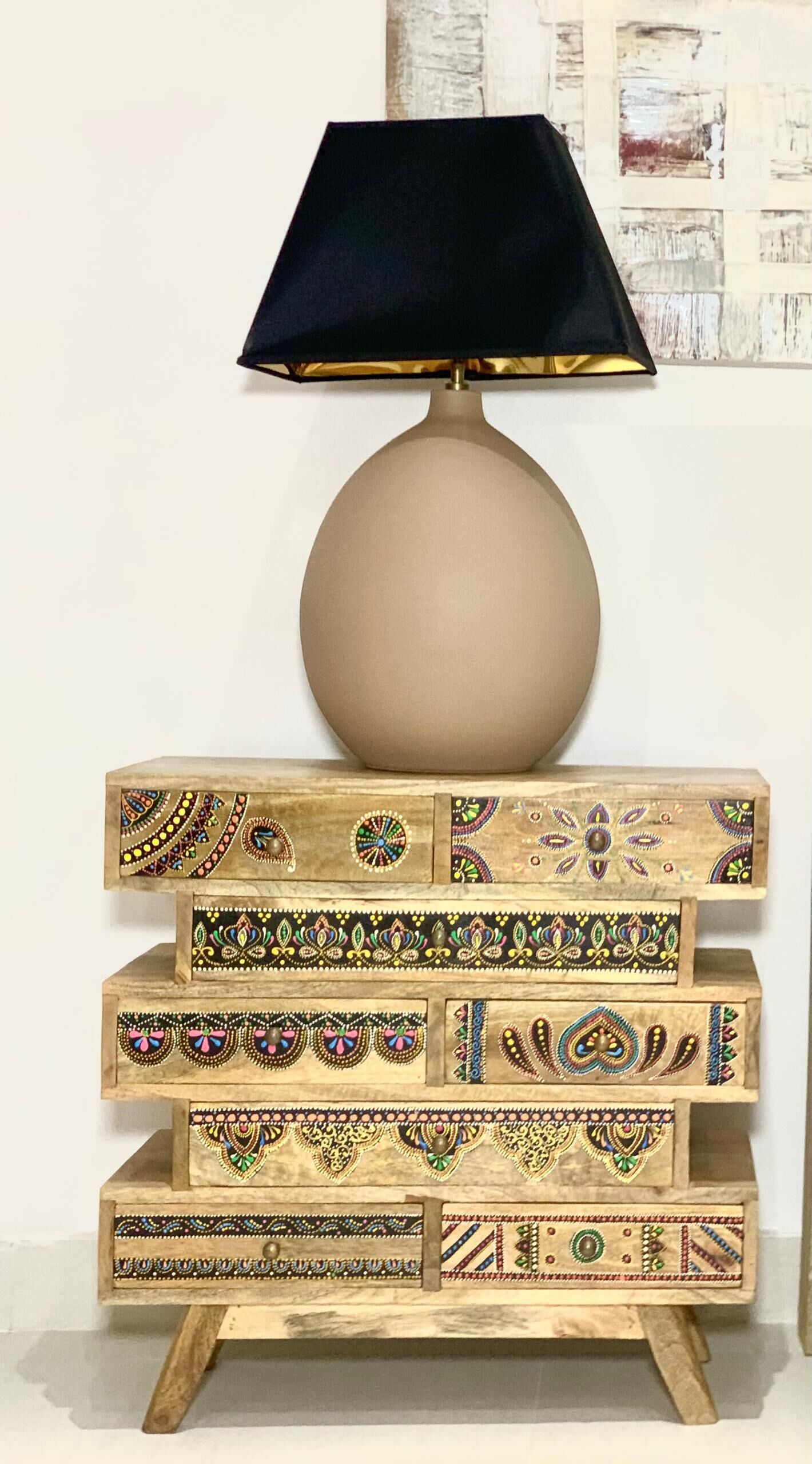 Een gelaagd nachtkastje van hout met ingewikkelde decoraties, een zwarte lampenkap en een ronde tafellamp.