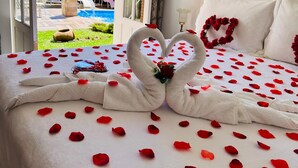 A bed with rose petals and a heart-shaped towel arrangement, a view of a swimming pool, and a patio area. - Pousada Pink Village  (Campos do Jordão)