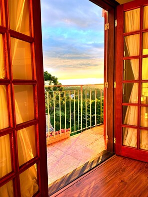 An open wooden door leading to a balcony with a view of a green landscape and a clear sky. - Pousada Pink Village  (Campos do Jordão)