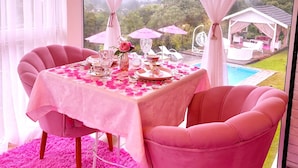 A room with a table set for two, pink chairs, a pink tablecloth, and a view of a pool and greenery outside. - Pousada Pink Village  (Campos do Jordão)