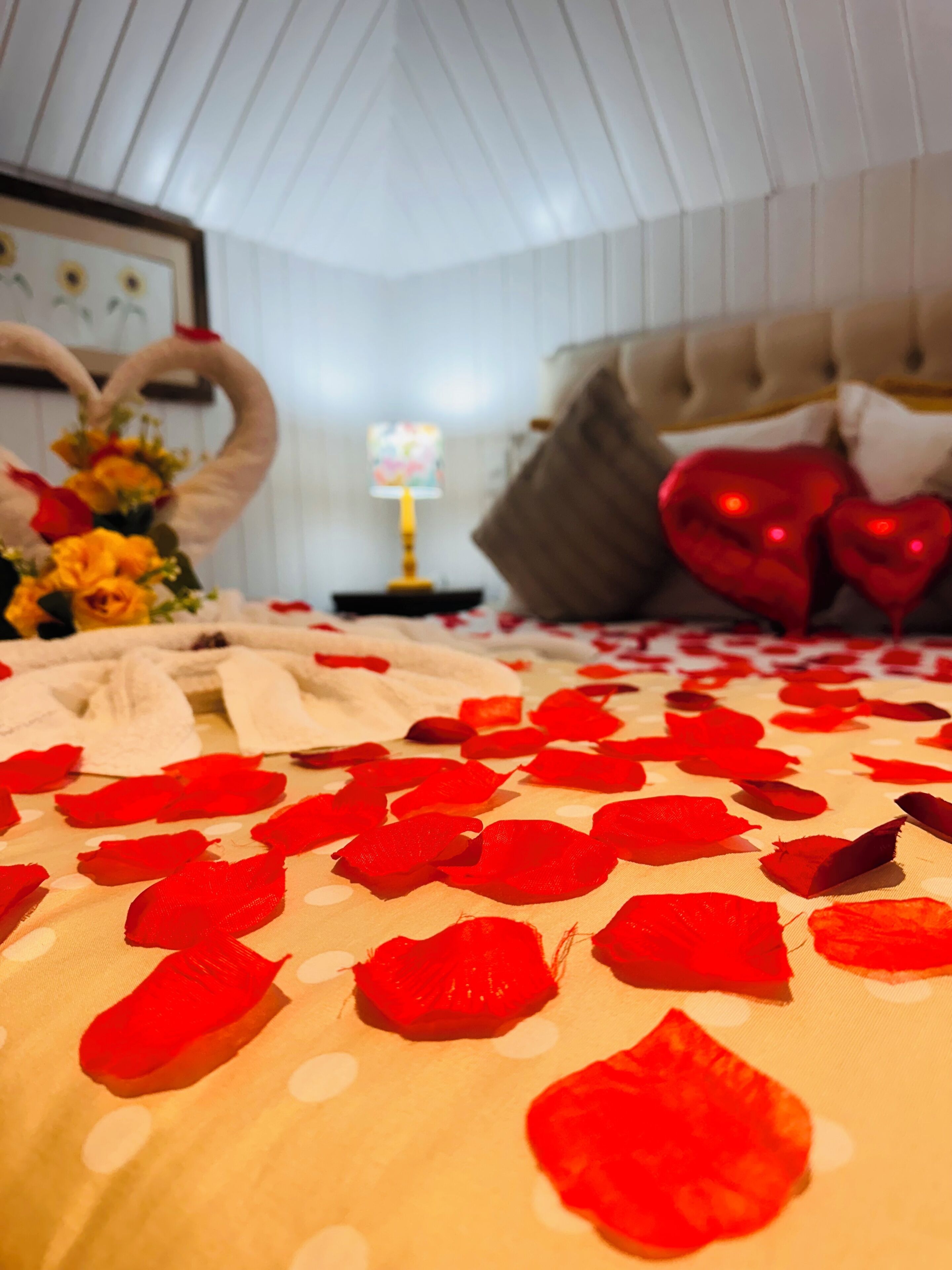 A bed with rose petals, a heart-shaped decoration, and a television in a room with a white ceiling and a sofa.