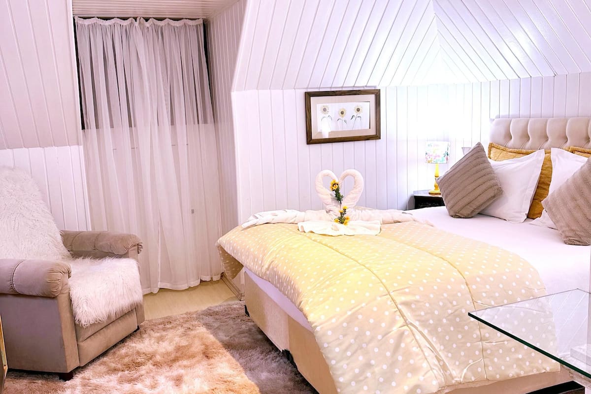 A bedroom with a bed, a chair, a window with curtains, and a framed picture on the wall.
