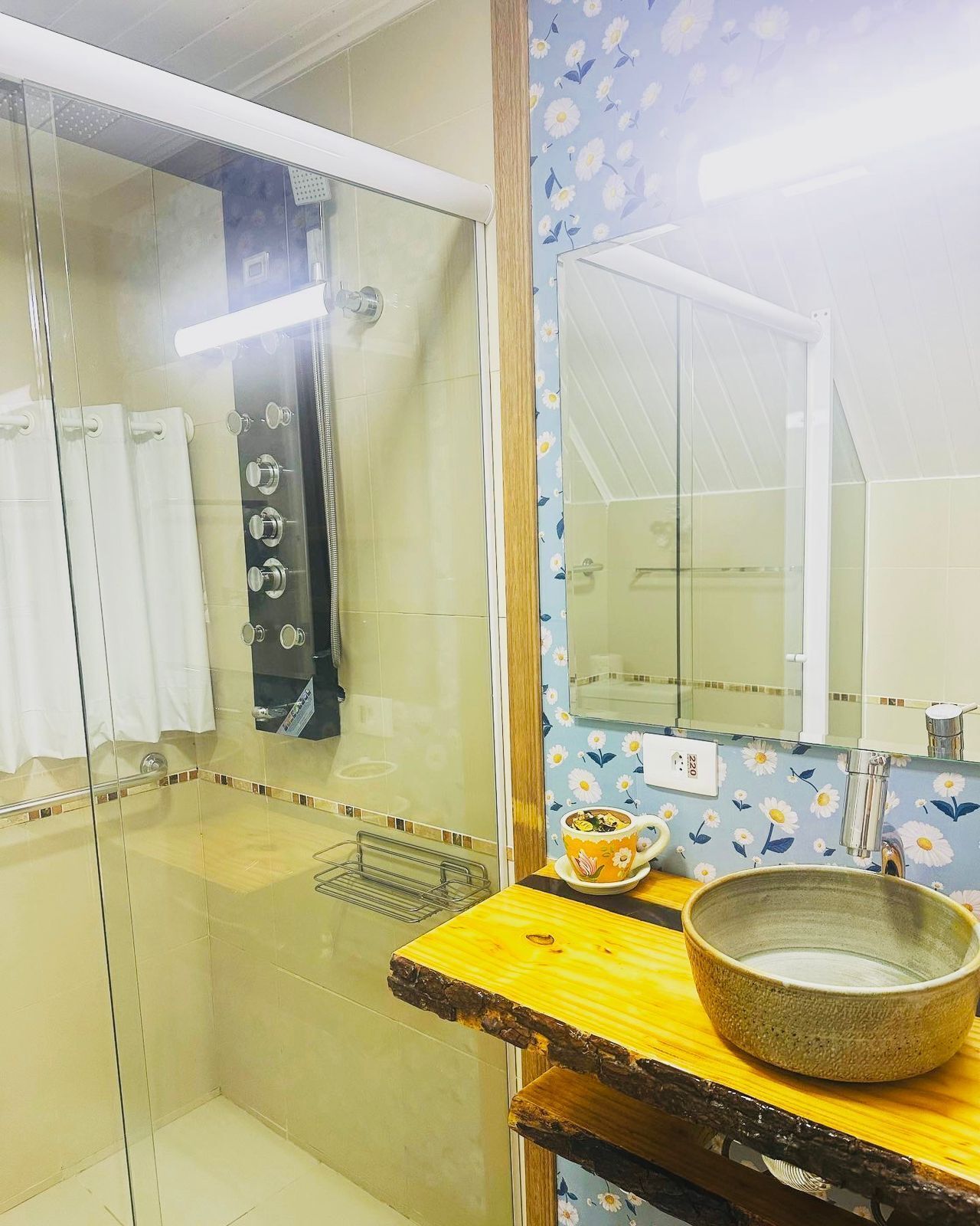 A bathroom with a glass shower enclosure, a wooden vanity with a bowl sink, and a mirror above the sink.