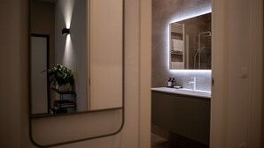 A modern bathroom with a mirror, sink, and shower. - Appartamento bilocale ARCADIA (Verona)