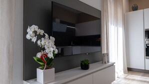 A modern living room with a flat-screen TV mounted on a wall, a potted orchid, and a small succulent on a white console. - Appartamento bilocale ARCADIA (Verona)