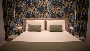 A bed with two pillows, a headboard, and a wall with a floral pattern. - Appartamento bilocale ARCADIA (Verona)