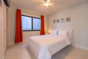 Una camera da letto con un letto, una finestra con tende, una ventola a soffitto e opere d'arte alle pareti.