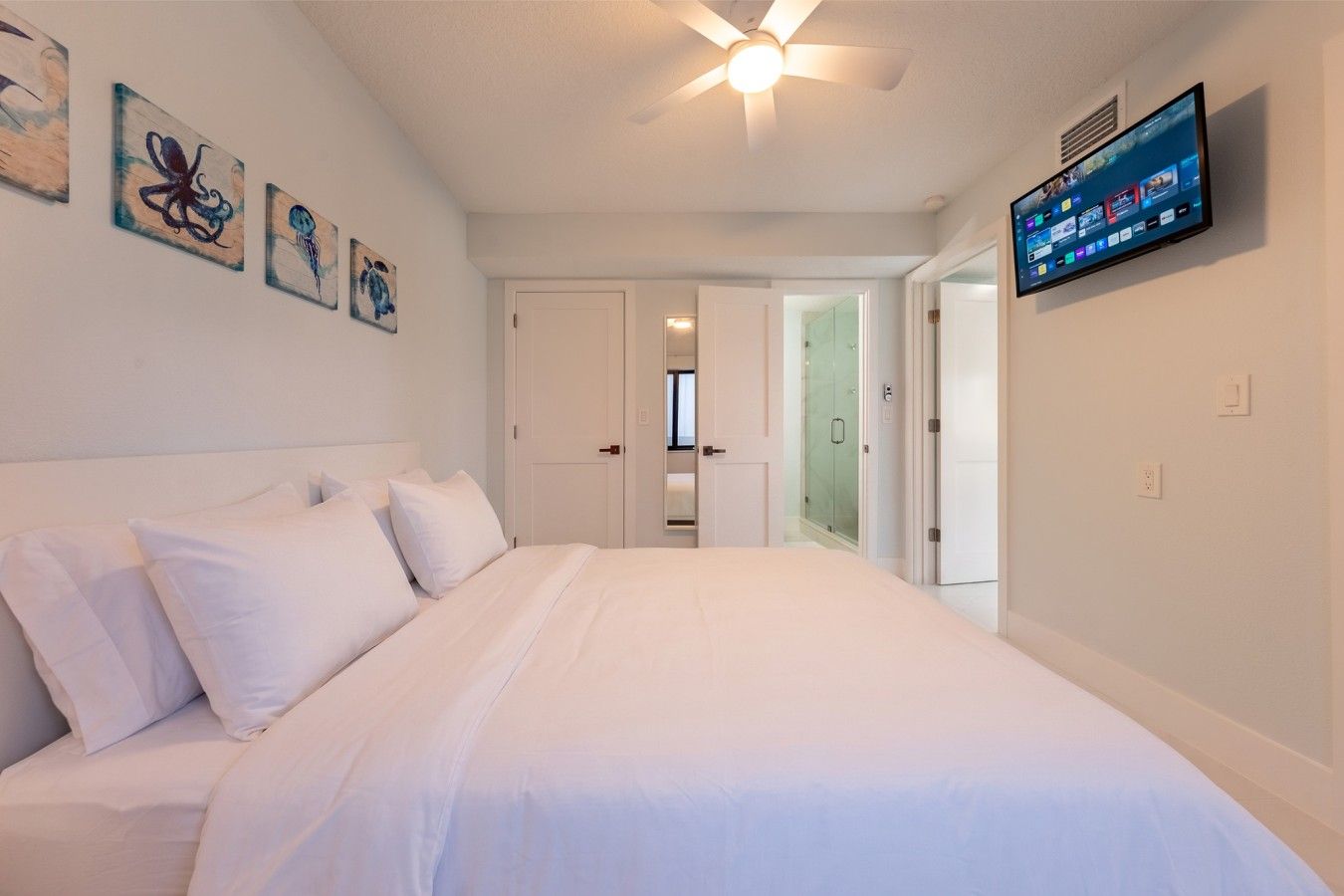 Ein Schlafzimmer mit einem Bett, einem Deckenventilator und einem an der Wand montierten Fernseher.