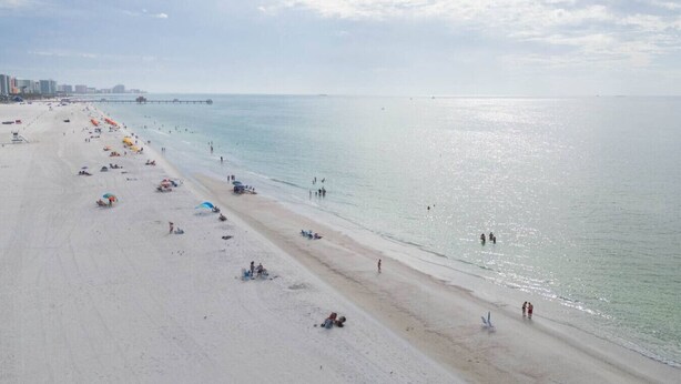 Ein weiter Strand mit einer Mole, die sich ins Wasser erstreckt, und einer Stadtlandschaft in der Ferne.