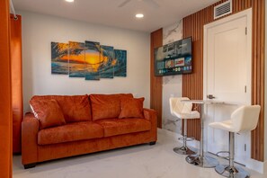 Un soggiorno moderno con un divano, due sgabelli da bar, una TV a parete e un quadro sopra il divano.