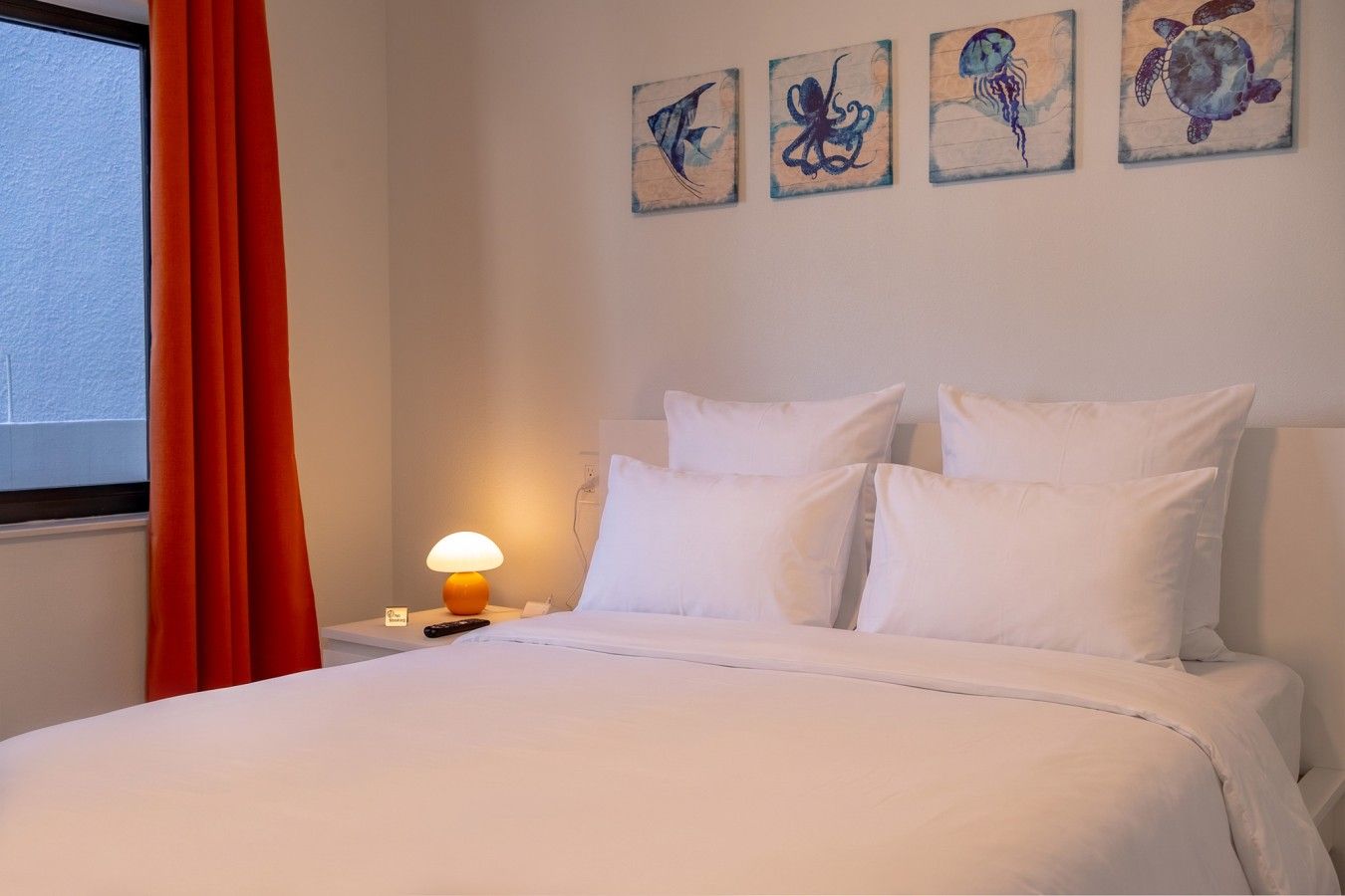 Une chambre d’hôtel avec un lit, des oreillers blancs, une table de chevet avec une lampe et des œuvres d’art accrochées au mur.