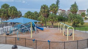Ein Spielplatz mit blauem Baldachin, Schaukeln und einer Kletterkonstruktion.