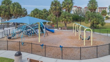 Ein Spielplatz mit blauem Baldachin, Schaukeln und einer Kletterkonstruktion.
