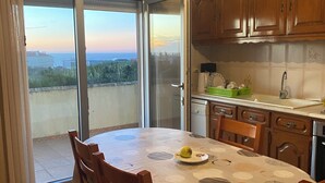 A dining area with a table set for four, a kitchen with wooden cabinets, and a sliding glass door leading to a balcony with a view of the sea. - The house on the Atlantic Ocean Portugal (Praia do Pedrogao)