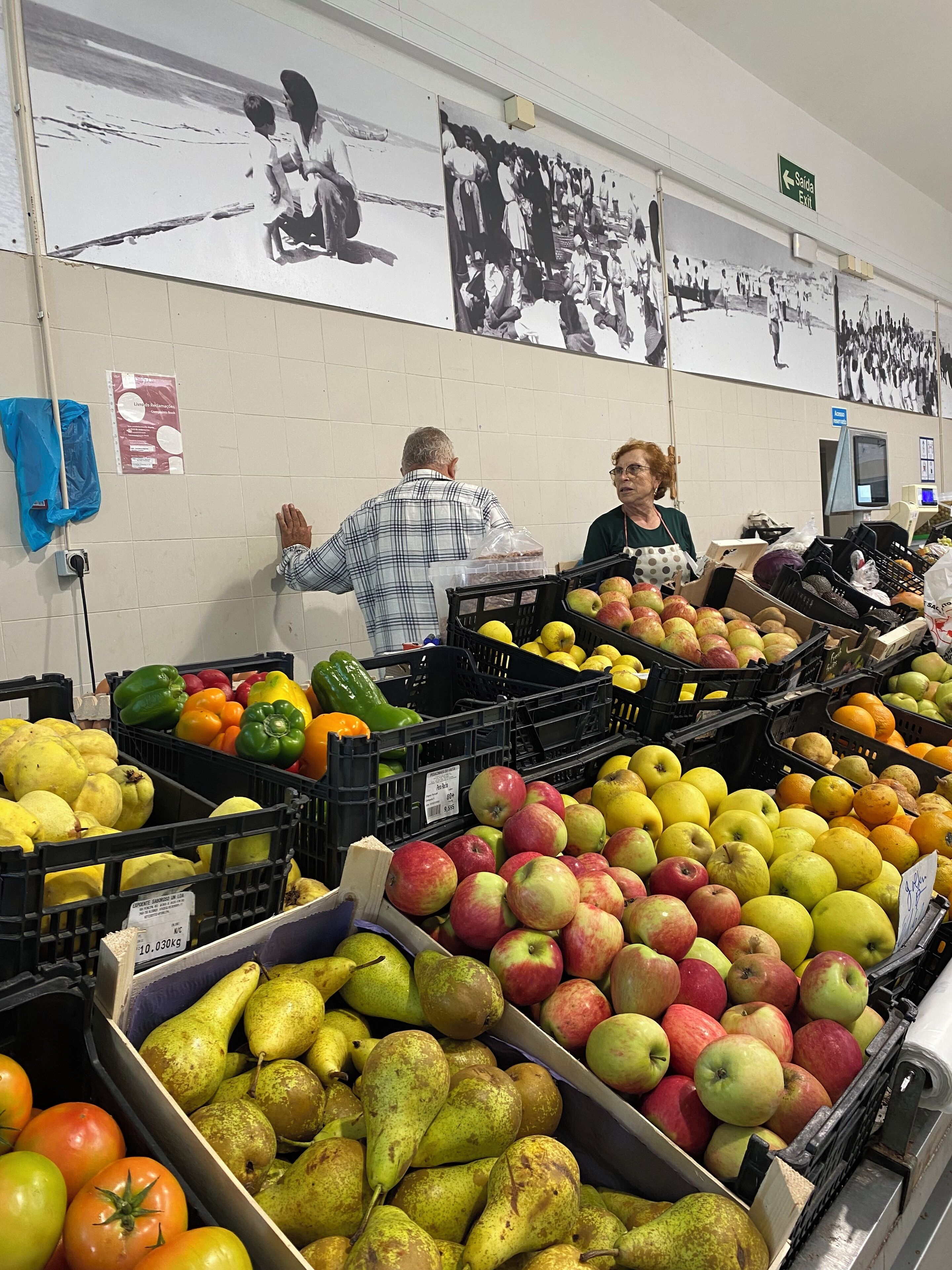 Een supermarkt met groenteafdelingen en een muur met zwart-witfoto's.