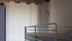 Camera con letto a castello, soffitto in legno, tende bianche e pavimento piastrellato.
