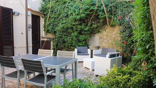 Patio esterno con tavolo e sedie, immerso nel verde e delimitato da un muro in pietra.