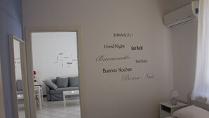 Una camera d'albergo con un letto, un comodino, una lampada e un muro decorato con cartelli bilingue con la scritta 'Buona notte'.