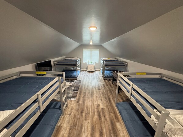 Une chambre de dortoir avec des lits superposés, un petit bureau et une fenêtre avec des stores.