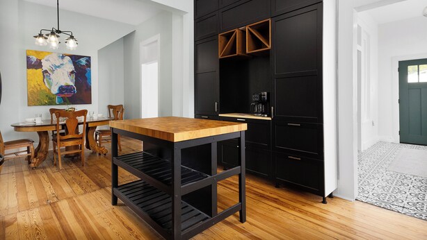 Una cocina moderna con muebles negros, una mesa de comedor de madera y un cuadro abstracto de colores.