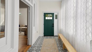 Un pasillo con piso estampado, una puerta verde y un banco.