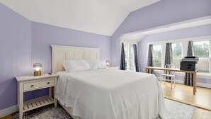 Un dormitorio con cama, mesita de noche, escritorio y ventanas amplias.