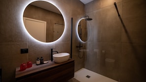 Un baño moderno con un espejo redondo, un lavamanos y una ducha.