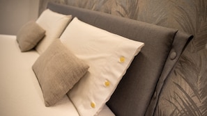 Una cama con cabecera gris y dos almohadas, una blanca y otra color beige.
