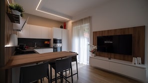 Una cocina moderna con encimera de madera, sillas negras, horno empotrado y televisor montado en la pared.