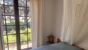 A room with a bed, a window with a view of trees, a small table with a lamp, and a chair. - Charm and relaxed living in Lorgues: Villa Tira, swimming pool and 3300 m2 garden (Lorgues)